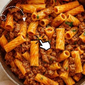 Close-up of rigatoni pasta with a rich, meaty tomato sauce and garnished with fresh herbs.