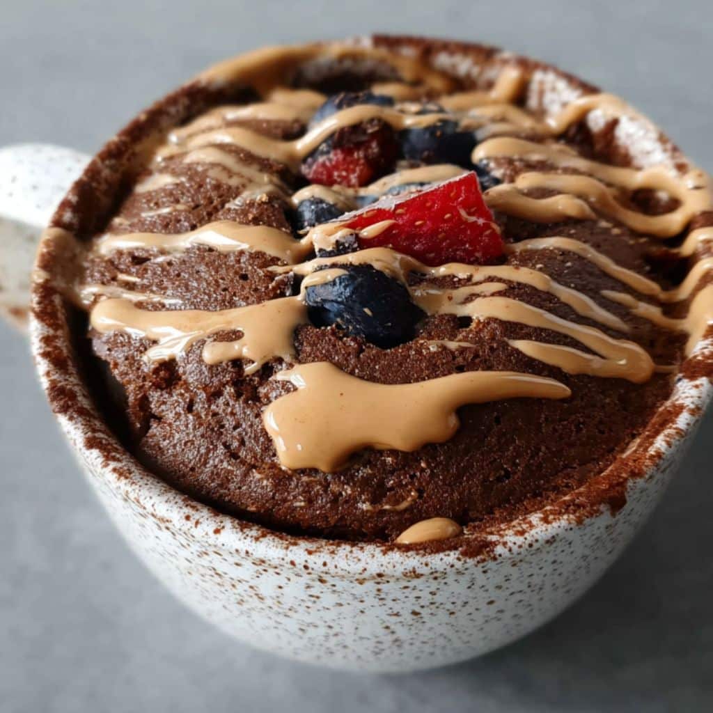 3 ingredient protein powder mug cake topped with peanut butter and berries