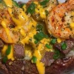 Steak and shrimp loaded potato topped with cheddar cheese sauce and green onions