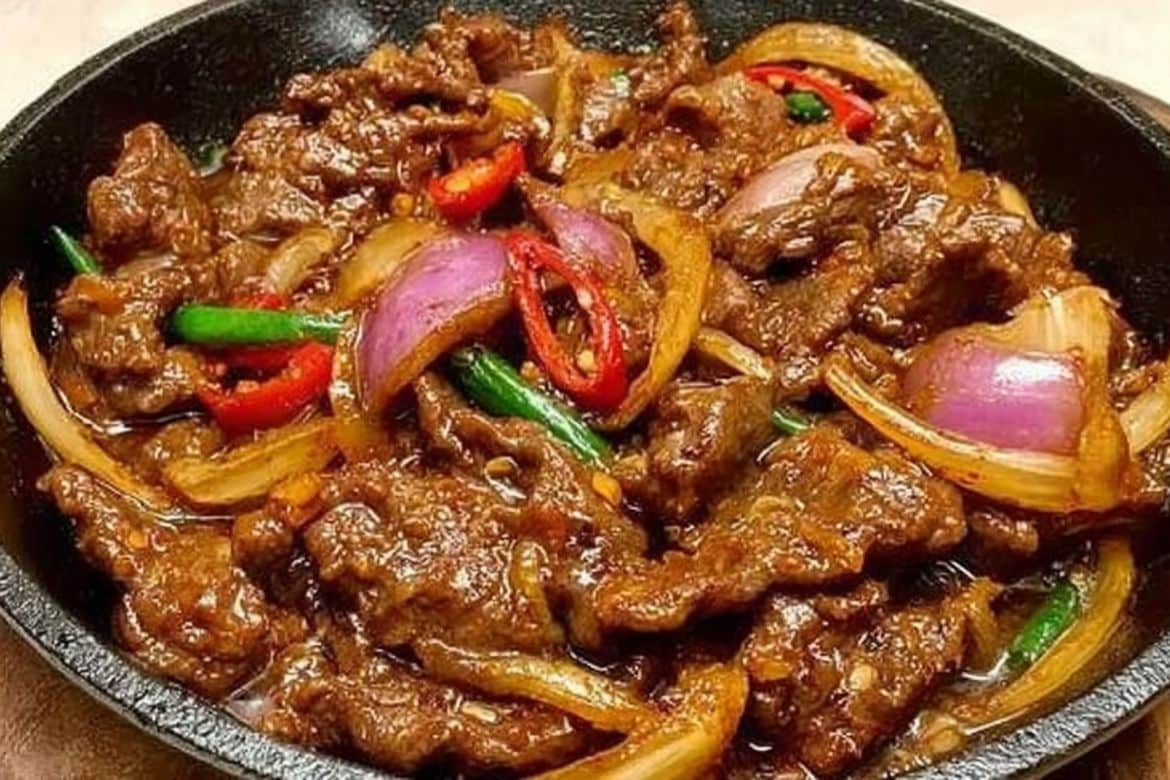 Stir-fried beef and onion recipe served hot in a skillet with red chilies and onions