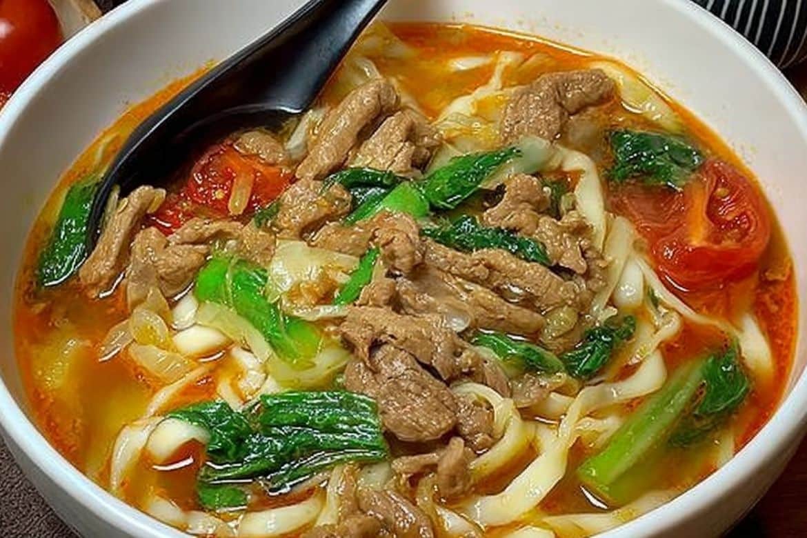 Tomato beef noodle soup with sliced beef, greens, and tomatoes in broth