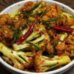 Close-up of spicy cauliflower stir fry with red chilies and scallions in a speckled ceramic bowl