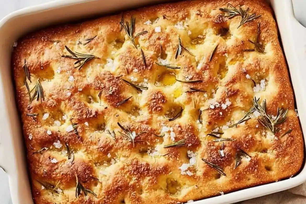 Golden baked focaccia bread with rosemary and sea salt in white baking dish