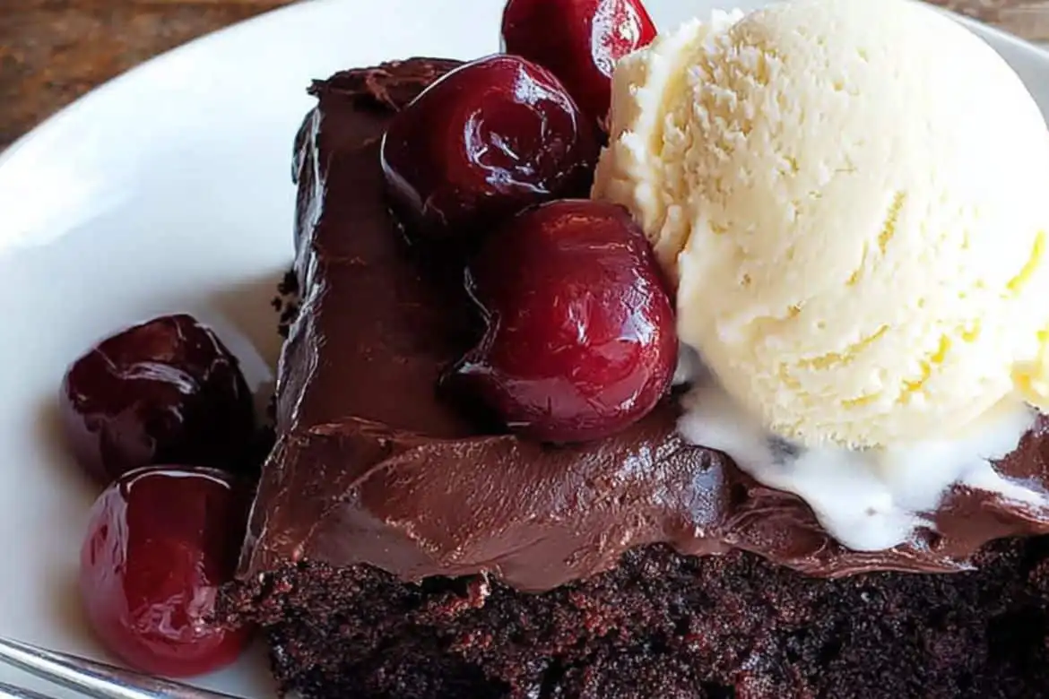 Slice of chocolate cherry cake topped with cherries and vanilla ice cream