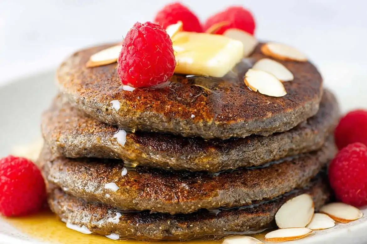 Stack of buckwheat pancakes with butter, raspberries, and sliced almonds