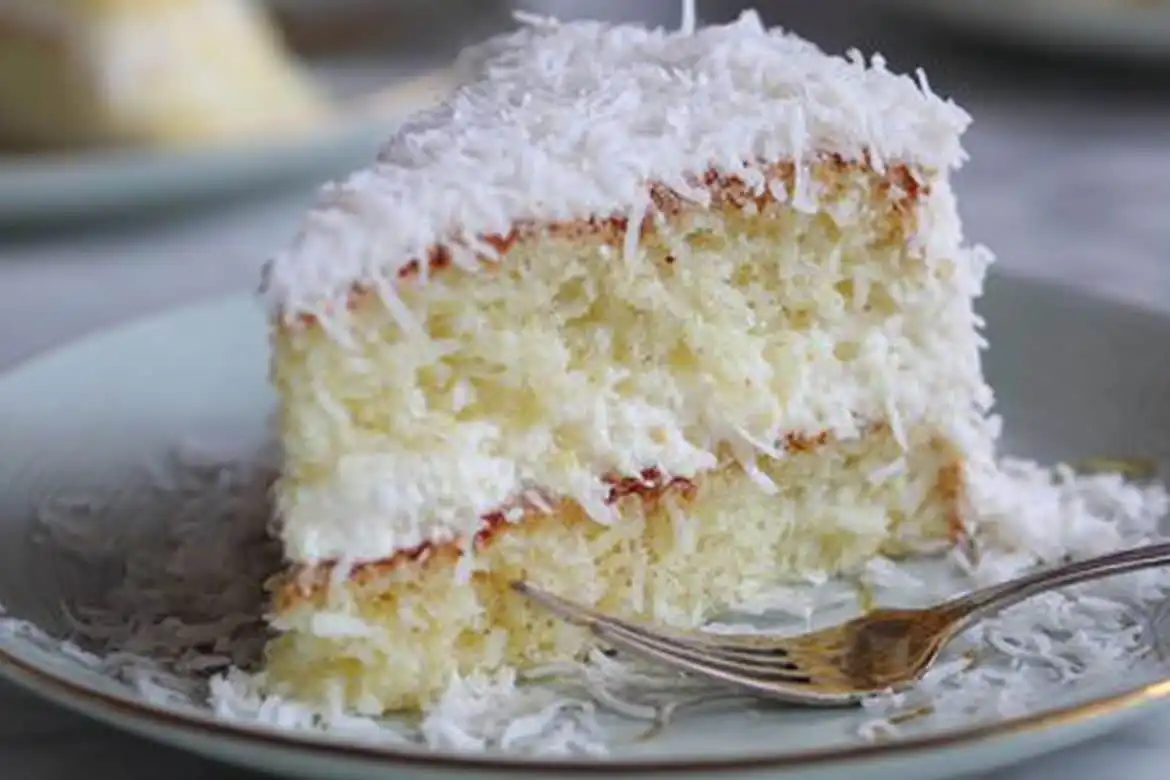 Slice of moist coconut cake using box mix with cream cheese frosting and coconut flakes