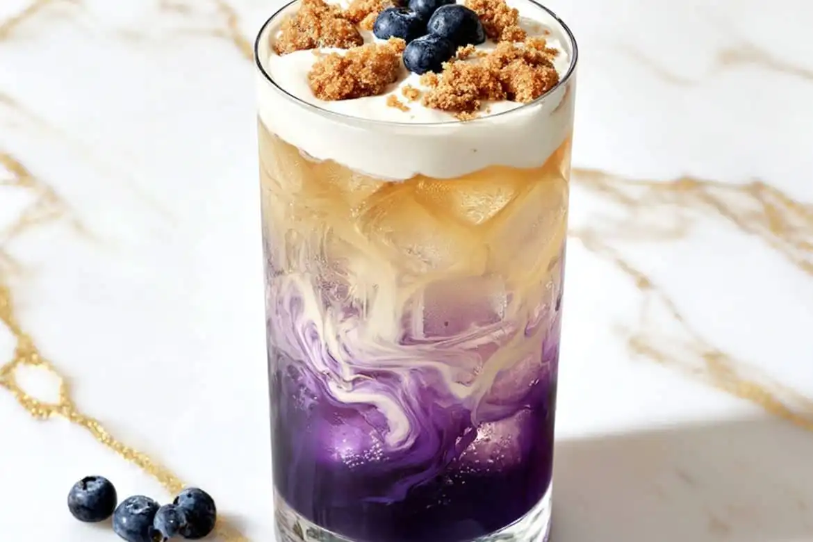 Blueberry Muffin Dirty Soda with ice, cream swirl, muffin crumbles, and blueberries in a glass
