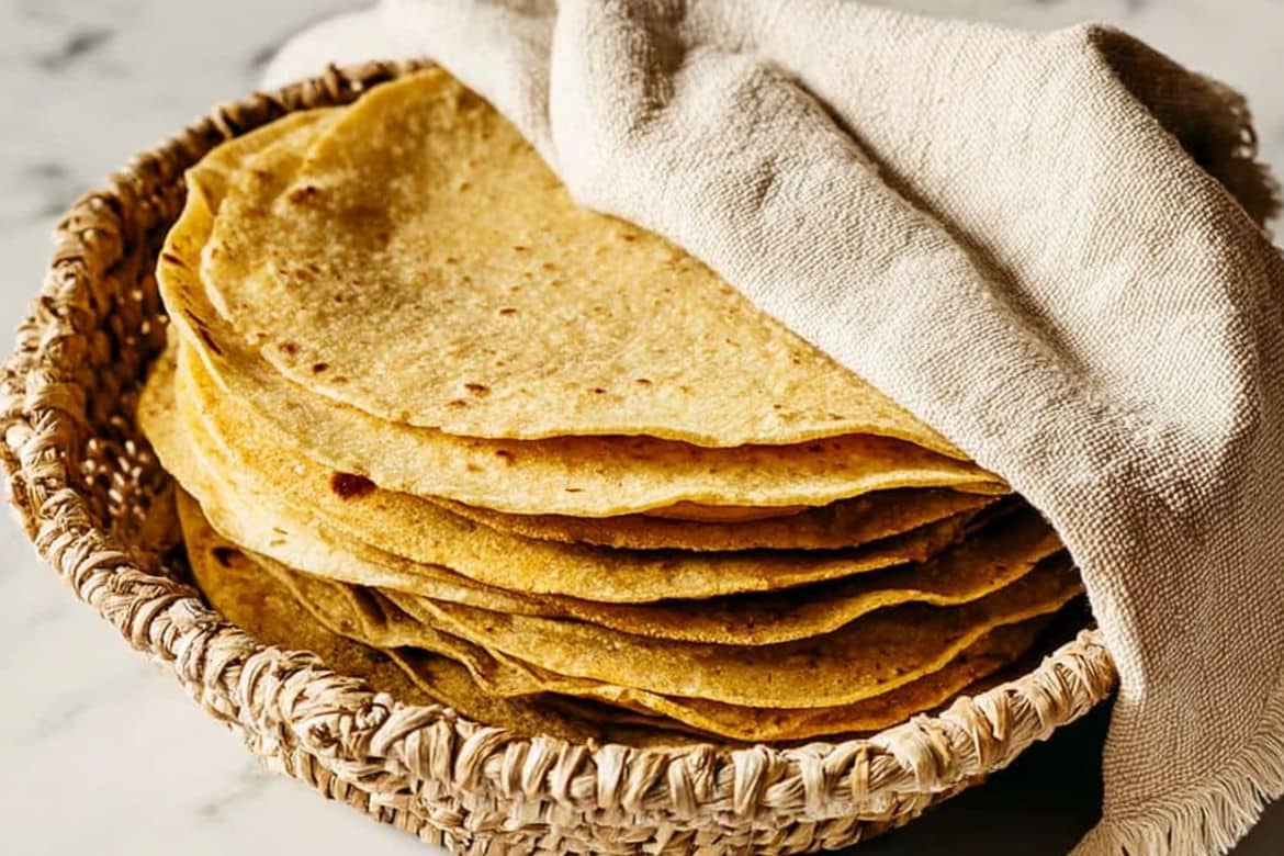 homemade corn tortillas stacked in a basket with towel