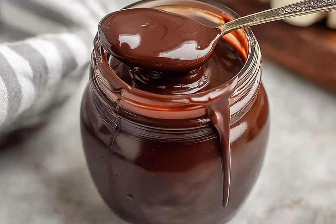 Spoon resting on a jar of hot fudge sauce with drips on the side