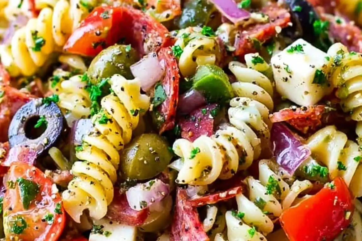 Pasta salad with Italian dressing made with rotini, salami, mozzarella, olives, peppers, and fresh herbs
