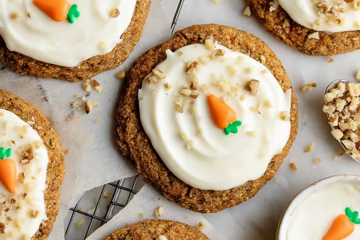 Carrot Cake Cookies topped with cream cheese frosting, chopped walnuts, and decorative carrot candy