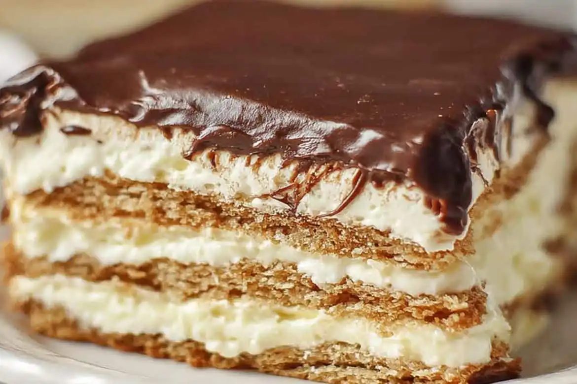 Chocolate eclair cake slice with layered graham crackers, creamy vanilla filling, and glossy chocolate frosting